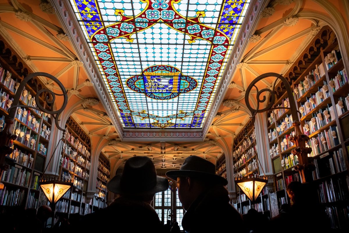 Interior of a Porto bookstore with stained glass ceiling and bookshelves.