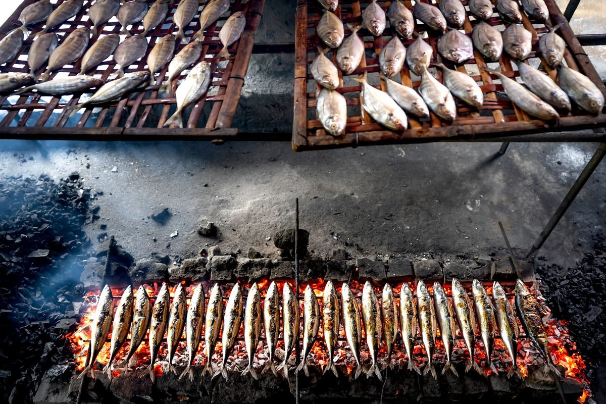 Fresh fish grilling over an open flame at a street food market.