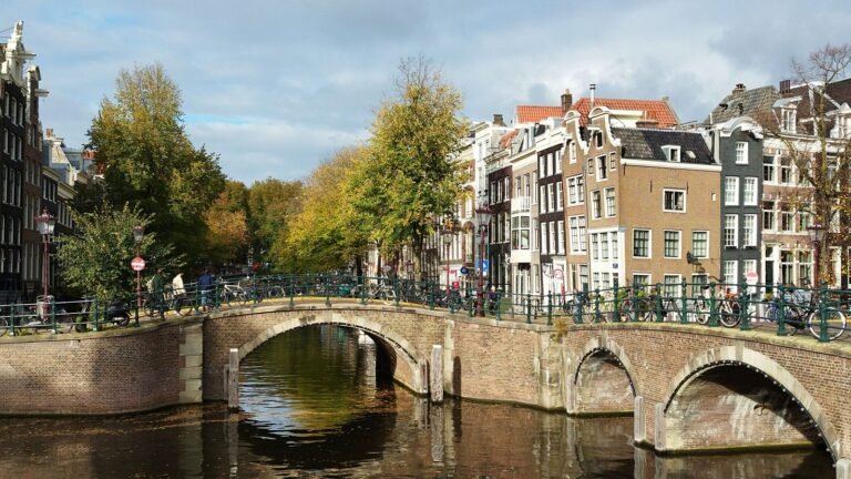 Canal scene with parked bicycles along a stone bridge and historic gabled houses in Amsterdam.