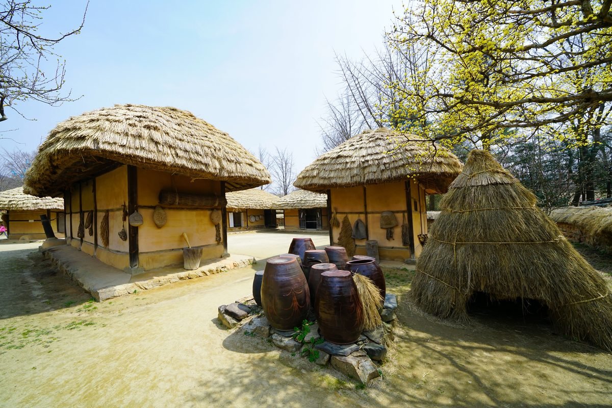 Traditional Korean village huts with straw roofs and large storage jars.