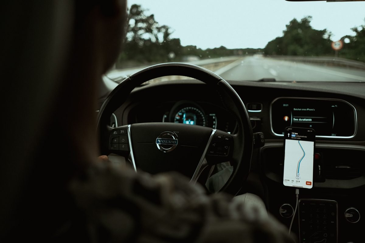 Driver's view from inside a car with a smartphone displaying GPS navigation.