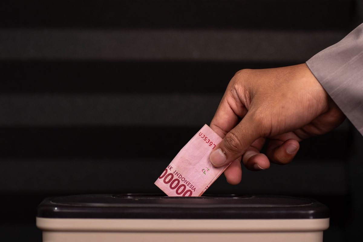 Hand placing an Indonesian Rupiah note into a donation box