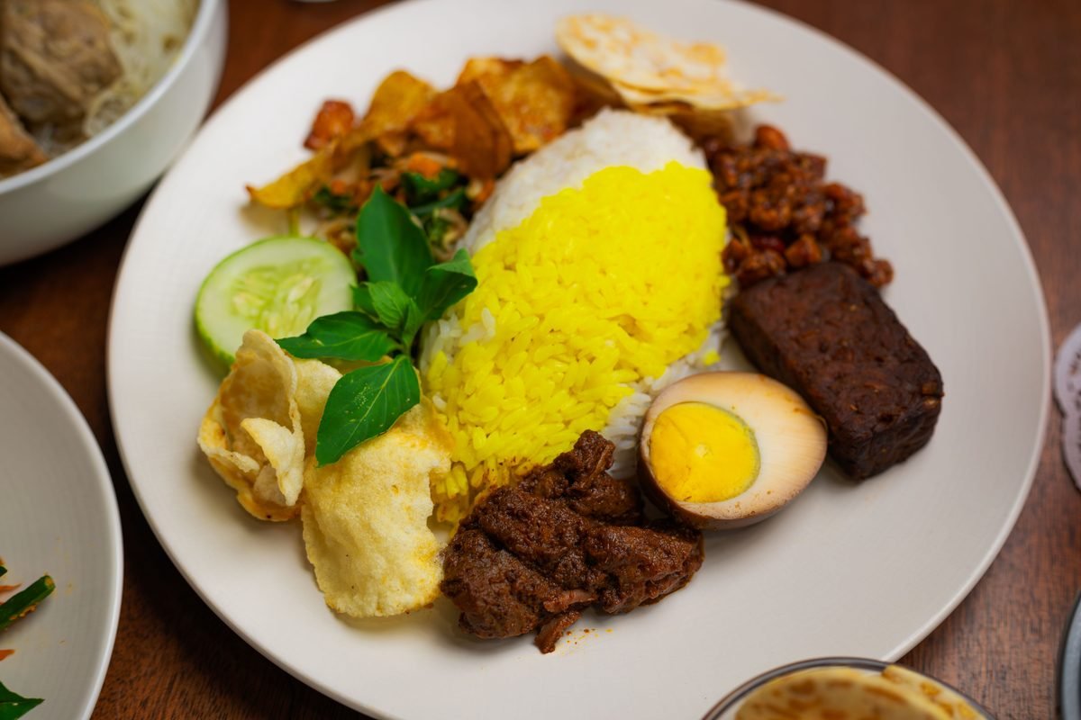 Plate of traditional Indonesian Nasi Campur with yellow rice and side dishes