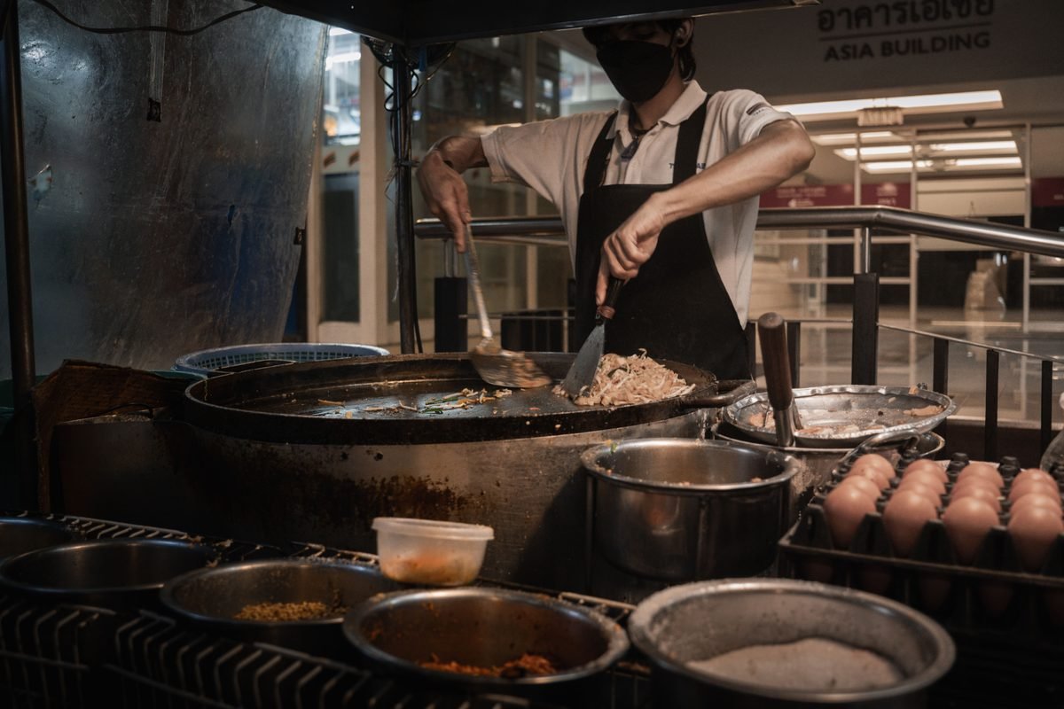 Masked street food chef cooking in a large wok at a night market
