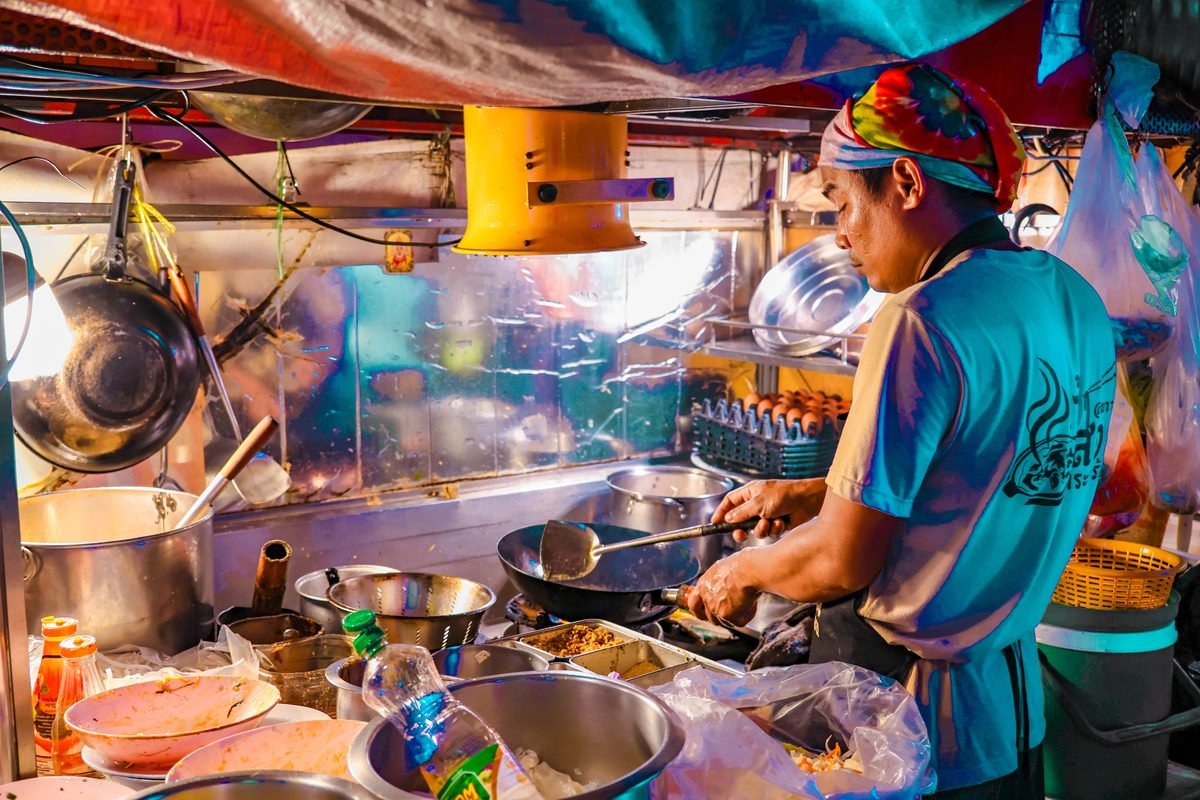 Vendor cooking in a street food cart with bright lighting