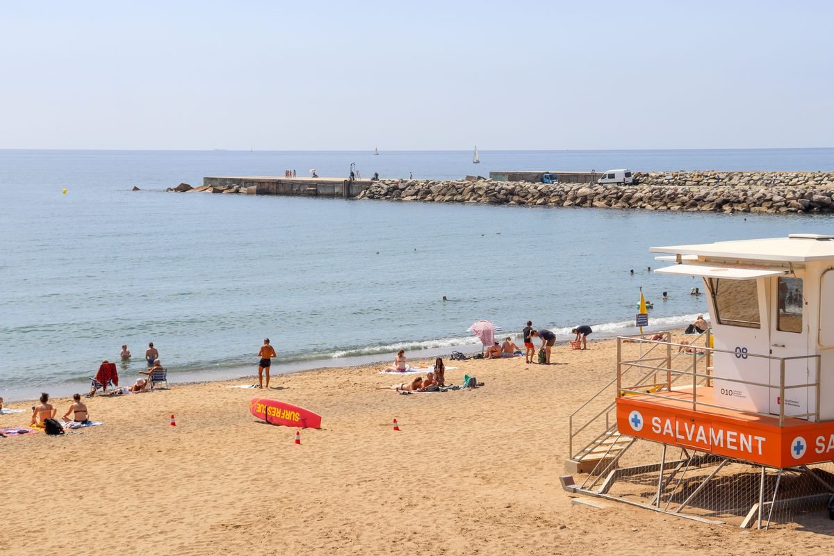 Sunbathers and a lifeguard tower on the sandy beach of Barceloneta in Barcelona.