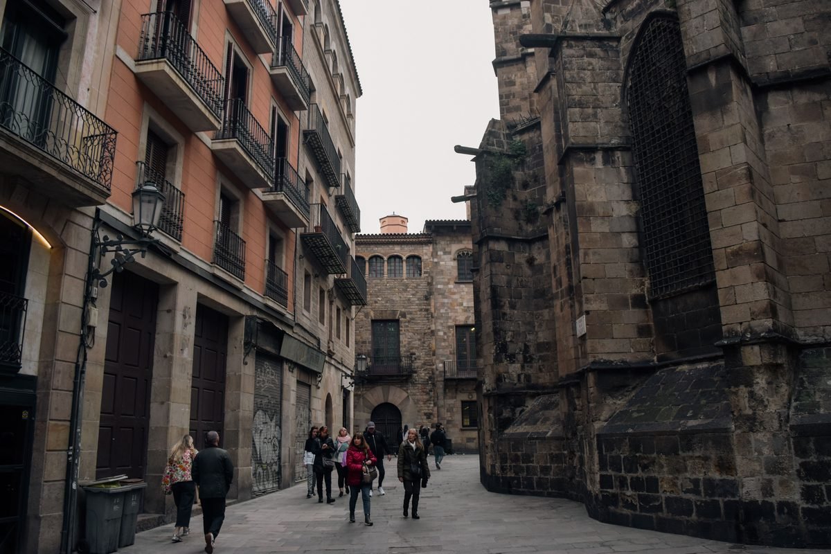 People walking through a narrow historic alleyway in the Gothic Quarter of Barcelona.