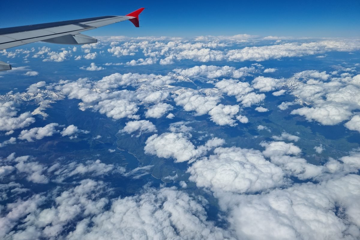 An airplane wing visible through a window, with a scenic sky and clouds outside.
