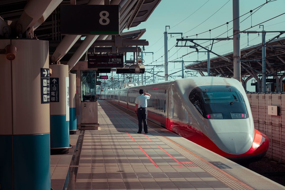 High-speed train waiting at a modern station platform with digital departure boards visible.