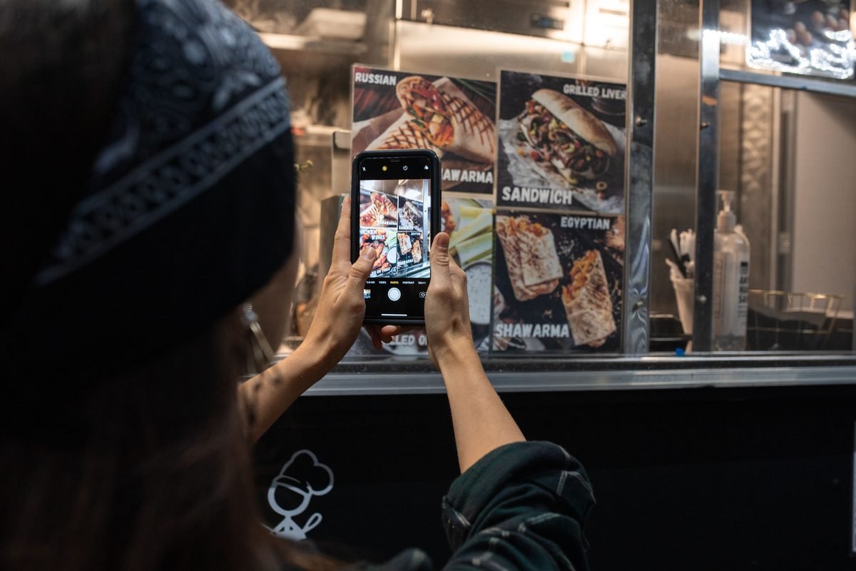 Person pointing a smartphone camera at a colorful street food menu written in foreign characters.