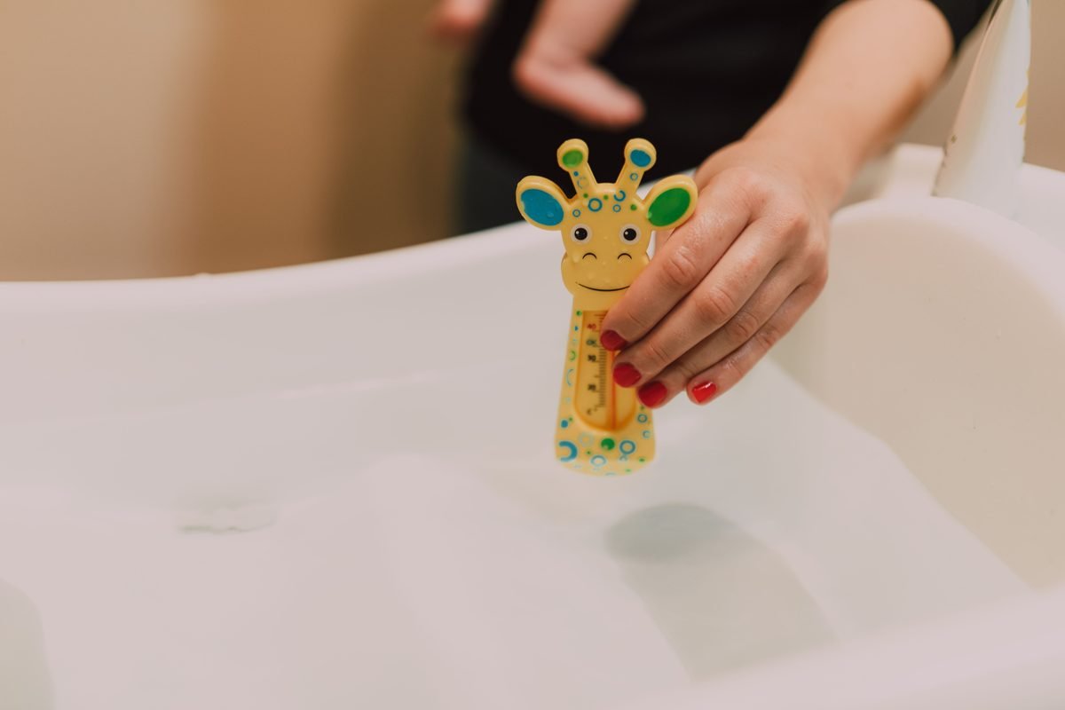 Hand checking water temperature with a toy thermometer in a tub