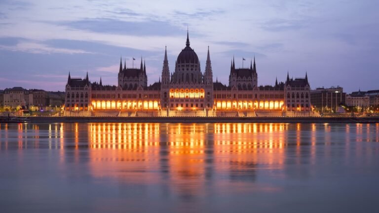 Hungarian Parliament Building illuminated at dusk alongside the Danube River in Budapest.
