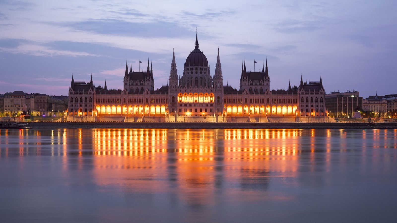 Hungarian Parliament Building illuminated at dusk alongside the Danube River in Budapest.