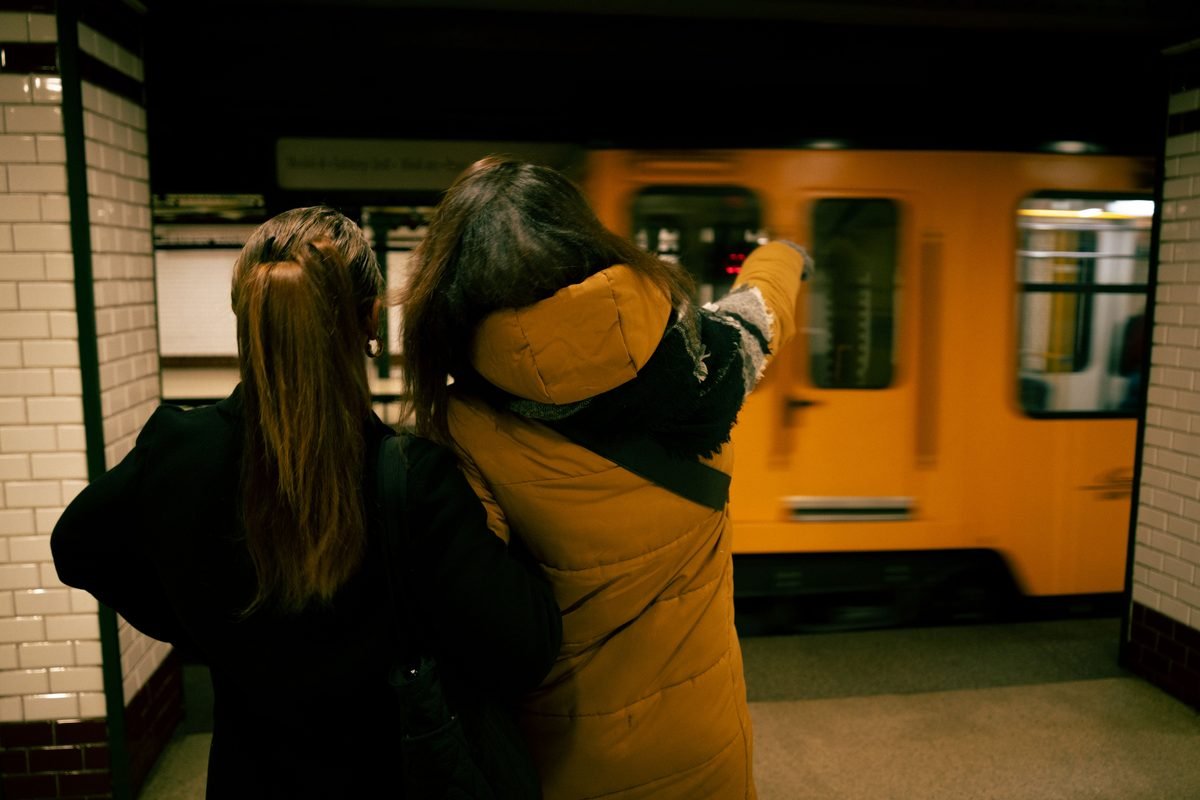 Two people waiting on a tiled platform for a yellow subway train