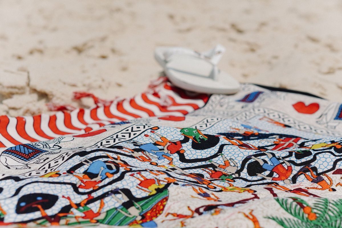 Patterned beach towel and a single sandal on sand