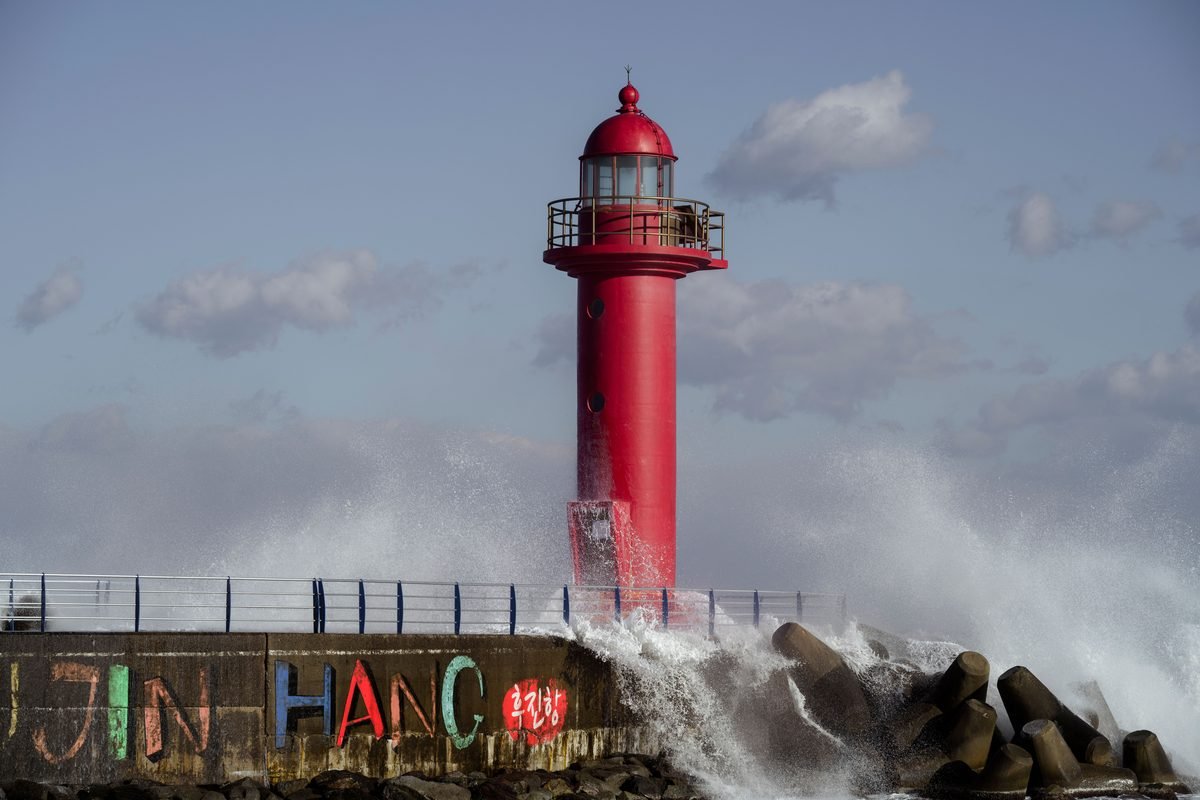 Vibrant red lighthouse standing on a concrete breakwater with splashing ocean waves