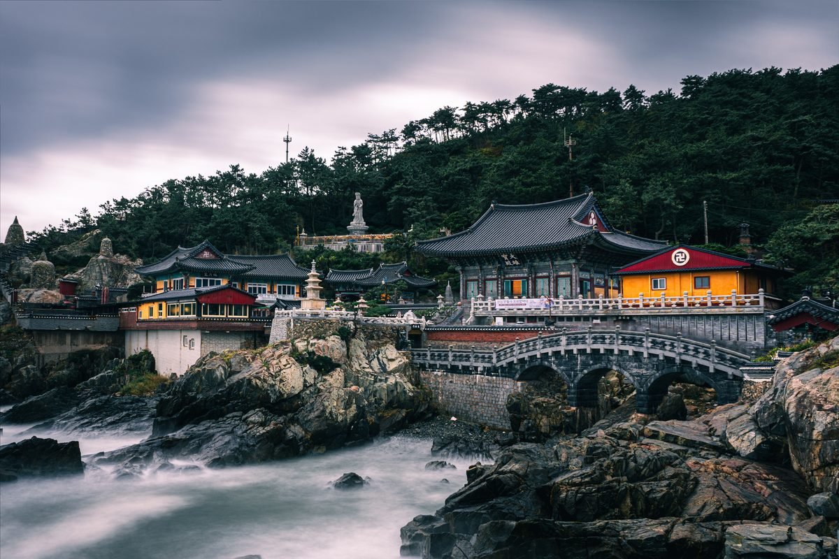 Traditional Korean temple architecture nestled on a rocky coastline with waves