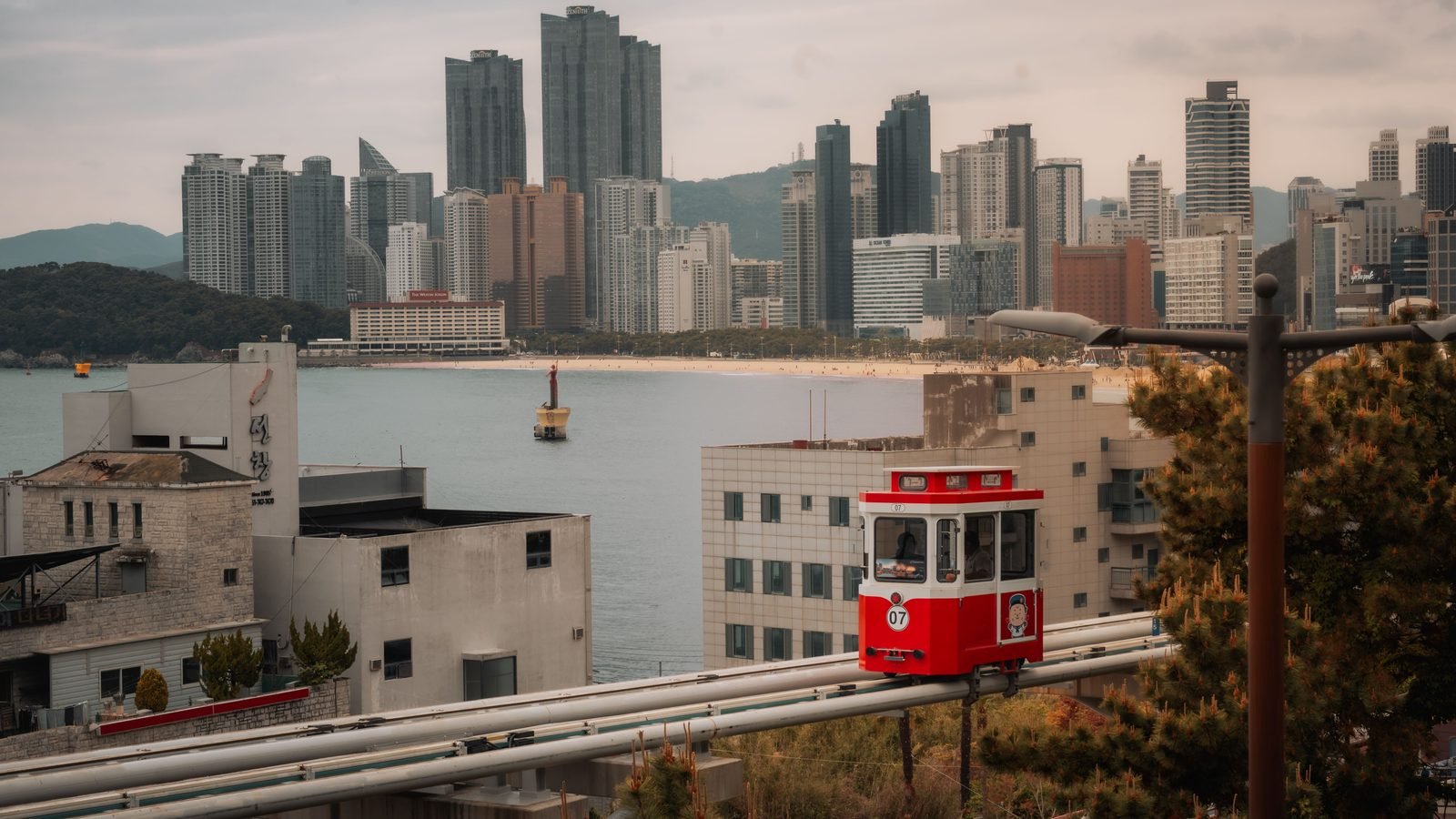 Red tourist tram car running on elevated rail overlooking urban skyscrapers and beach
