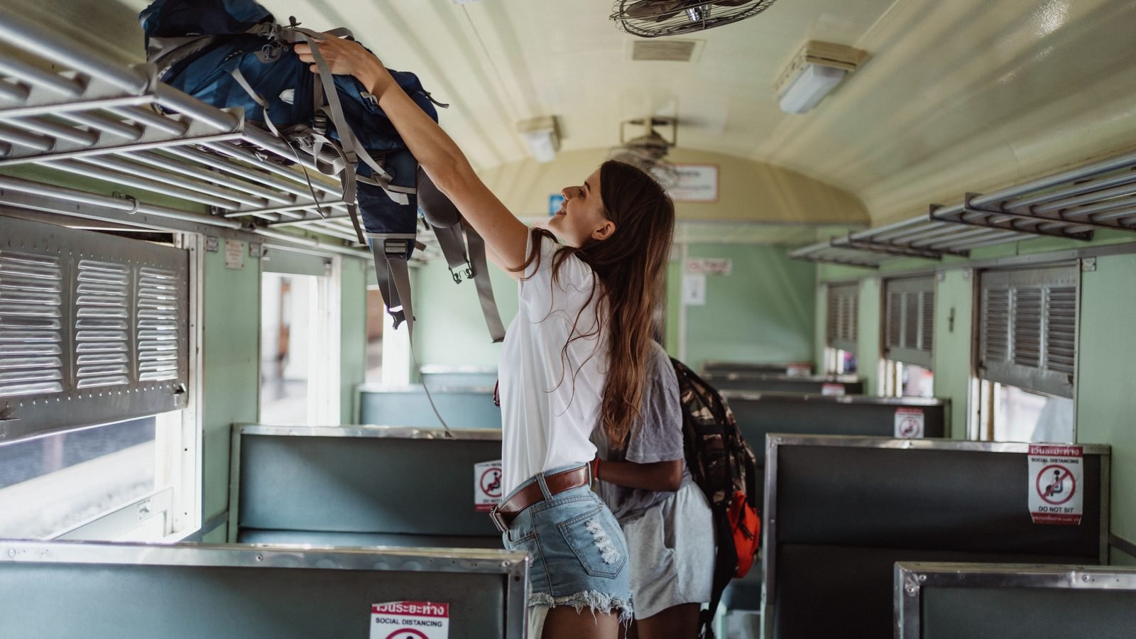Woman placing backpack on a luggage rack inside a train carriage