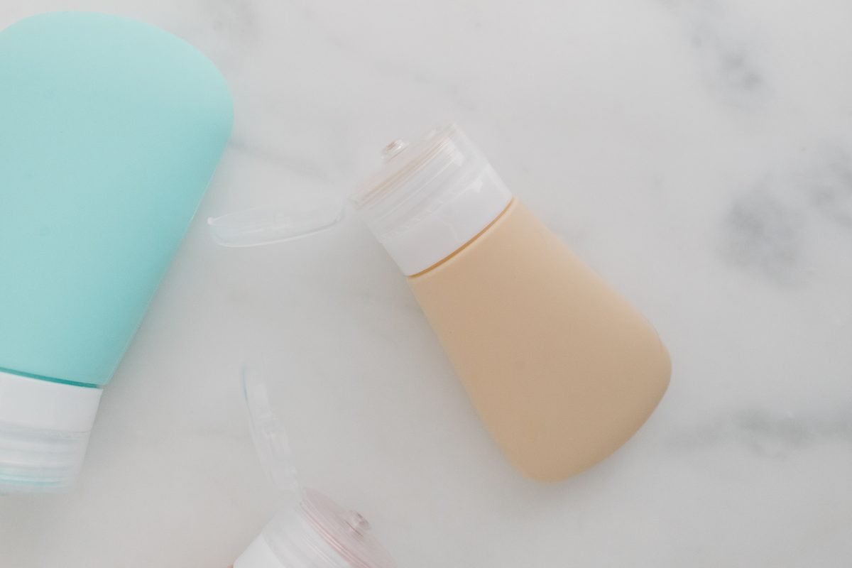 Soft-colored squeezable travel bottles with flip-top caps on a marble surface