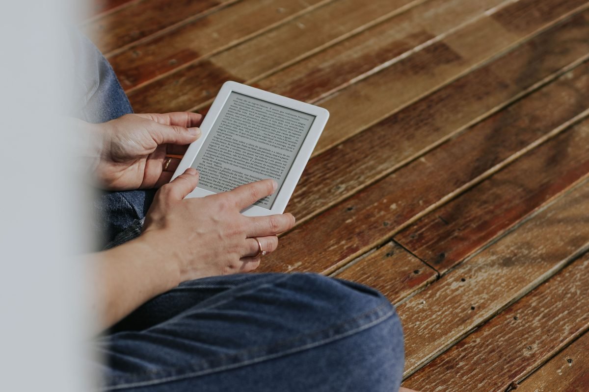 Close-up of hands holding an e-reader on a wooden floor