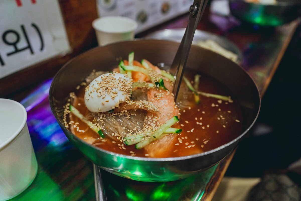 A close-up of Korean cold noodles topped with sesame seeds and vegetables.