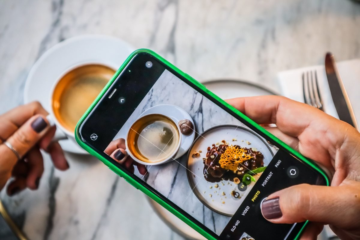 A smartphone photographing coffee and dessert in a restaurant.