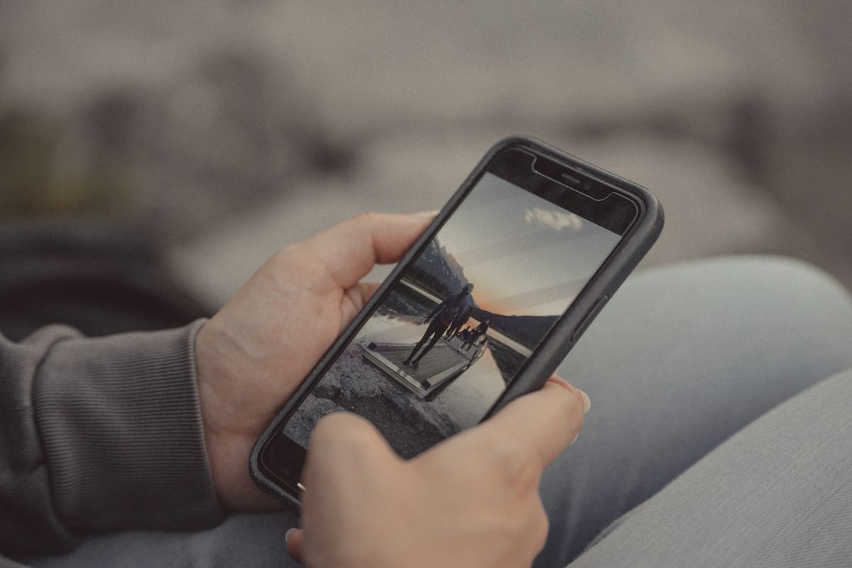 Hands holding smartphone displaying a mountain landscape photo.
