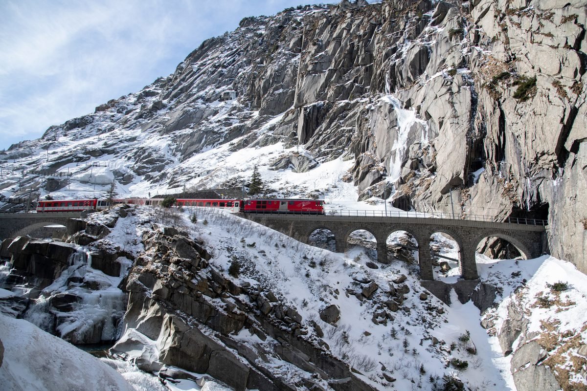 Red train crossing a snowy alpine viaduct in winter.