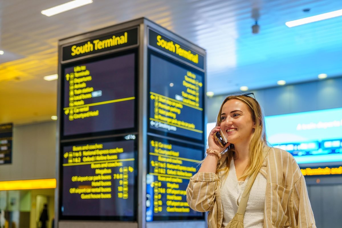 Smiling woman talking on phone near airport terminal display.
