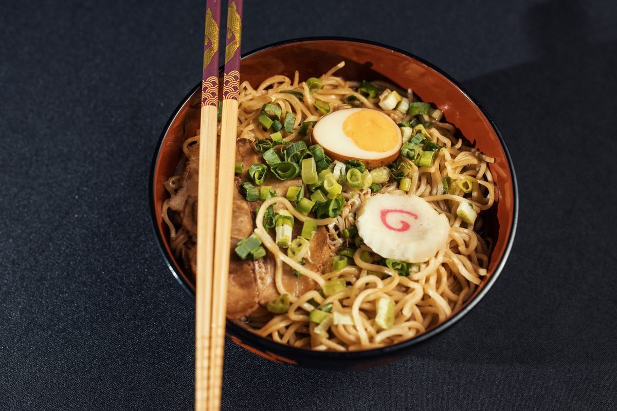 Bowl of ramen with green onions, egg, and chopsticks.