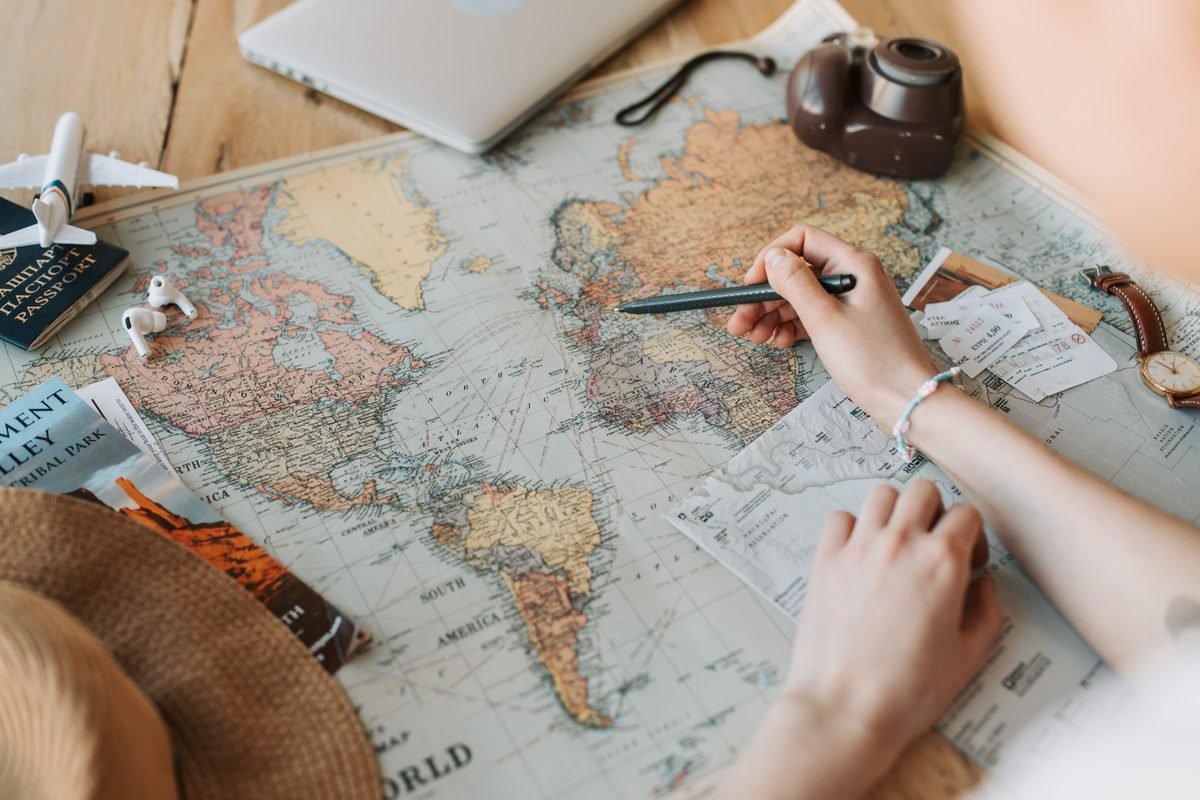 Hands marking destinations on a world map with travel essentials