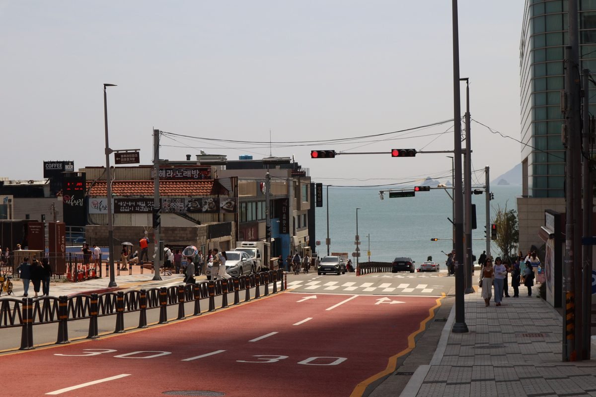 Steep coastal road leading down to the sea in Busan with Hangul signage.