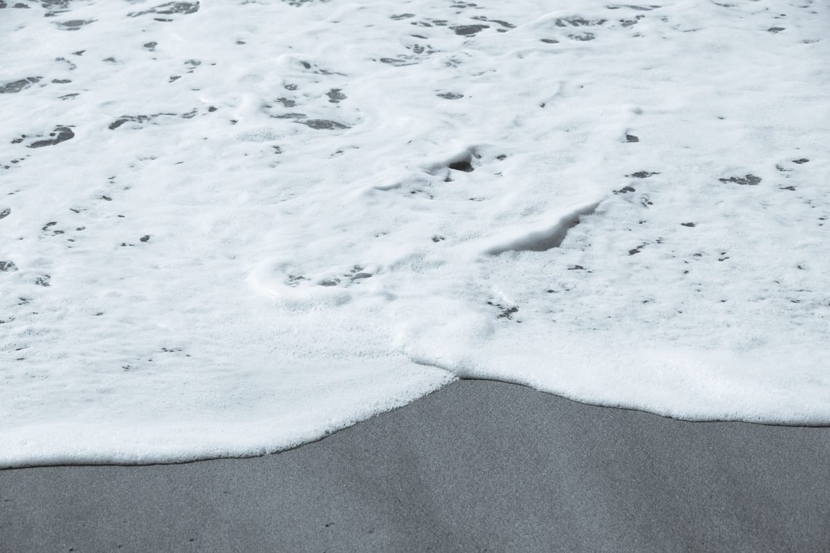 Close-up of white ocean foam washing onto a sandy shore