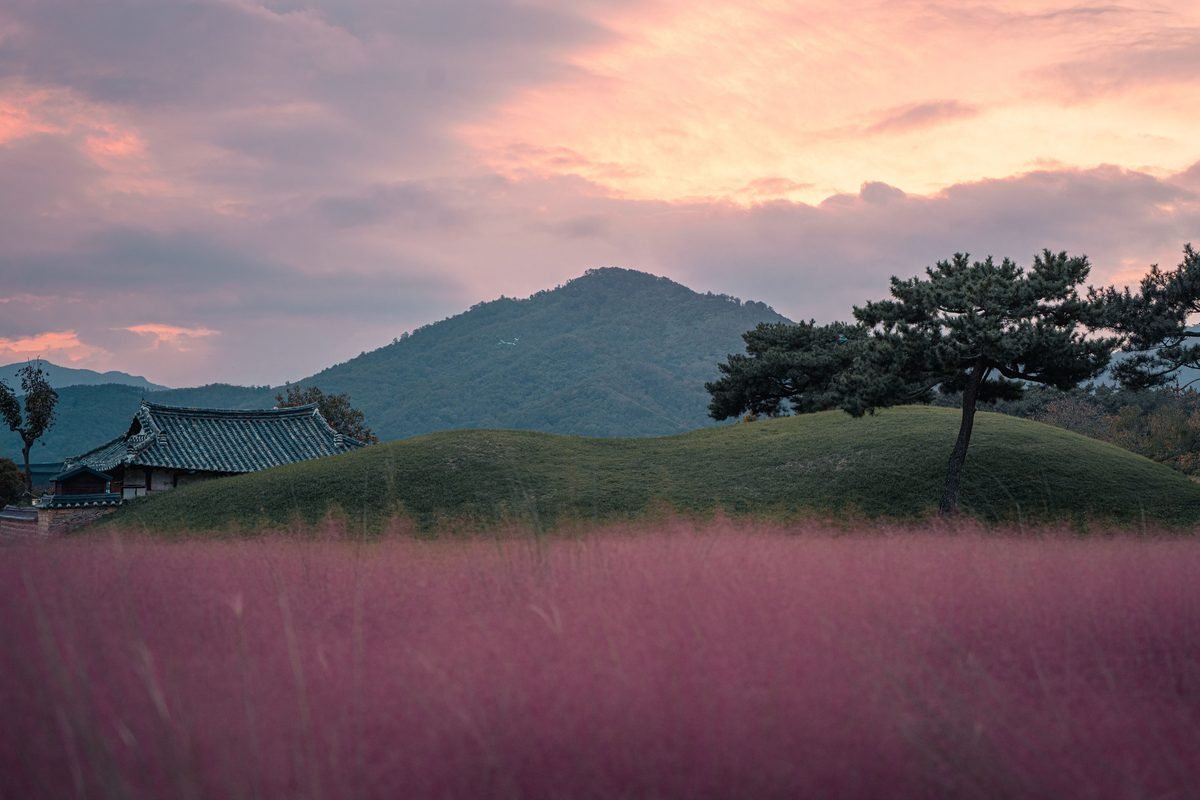 Traditional temple architecture next to an ancient royal tomb mound under autumn sunset in Gyeongju