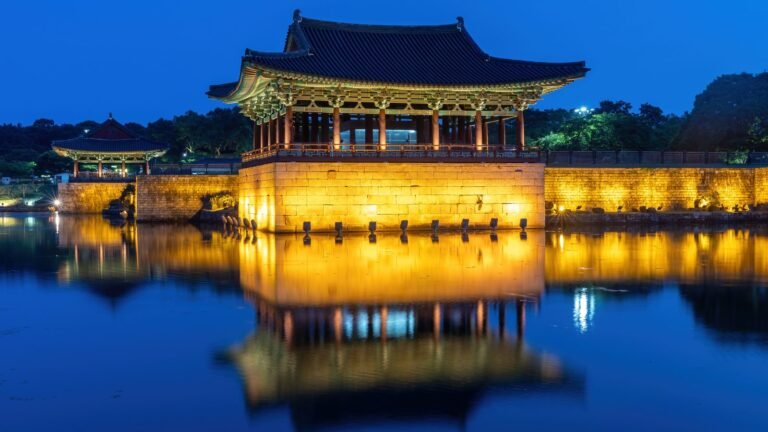 Illuminated wooden pavilion reflecting perfectly on the dark water of Wolji Pond at dusk in Gyeongju