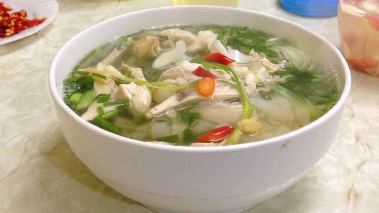 Bowl of pho ga chicken noodle soup with herbs and chili at a Hanoi street stall