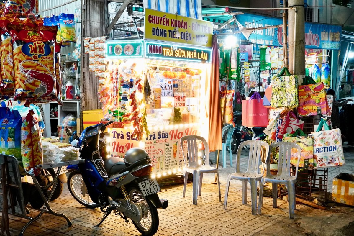 Night market stall with illuminated signs, snacks, and plastic chairs