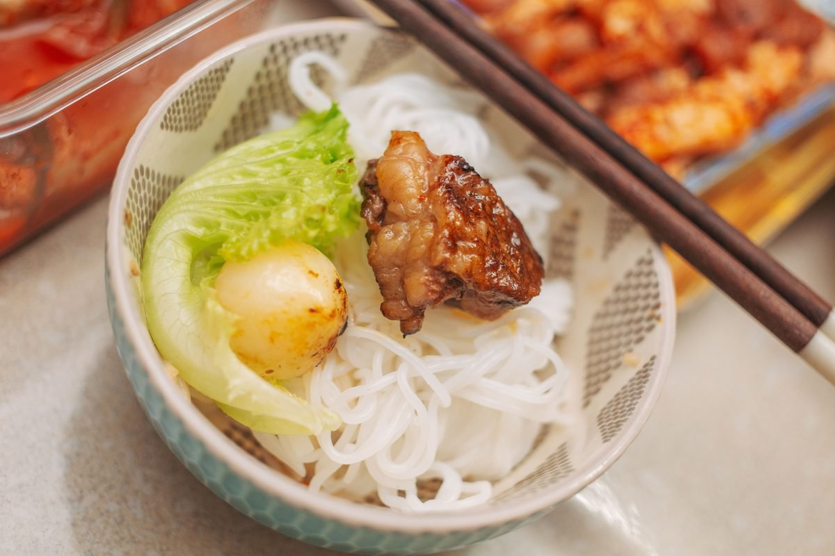 Bowl of white rice noodles with pork and lettuce served with chopsticks