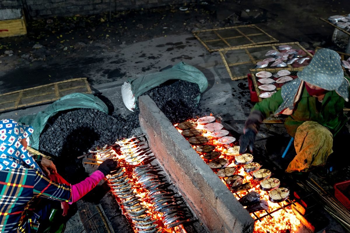 Outdoor street food vendor grilling fish and meat over hot charcoal