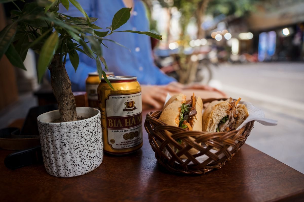 Canned beer and fresh banh mi sandwich on a street cafe table