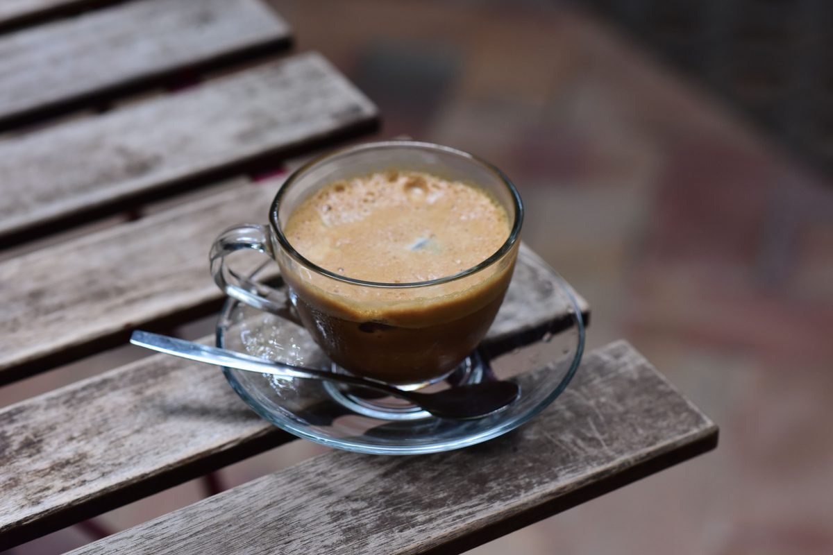 Glass mug filled with frothy coffee sitting on a wooden surface