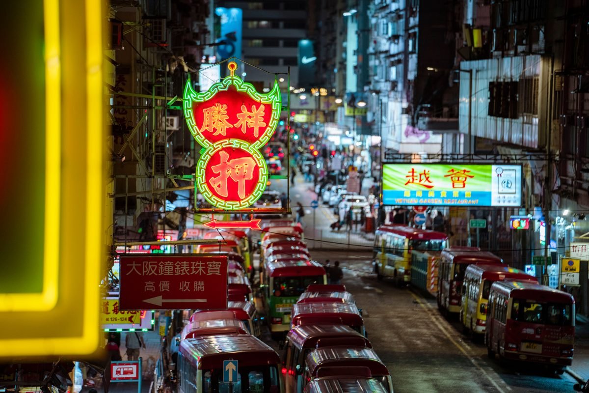 Vibrant Hong Kong street with red neon signs and minibuses at night.