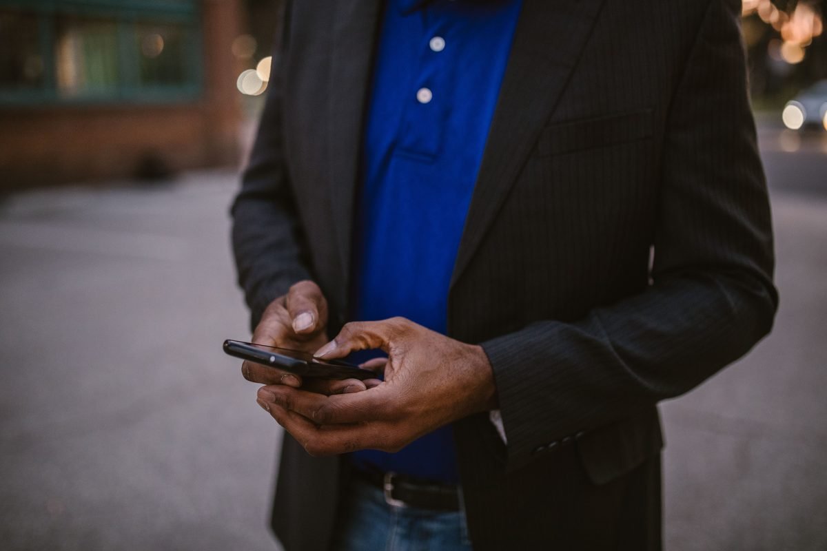A man in a black suit using a smartphone outdoors.