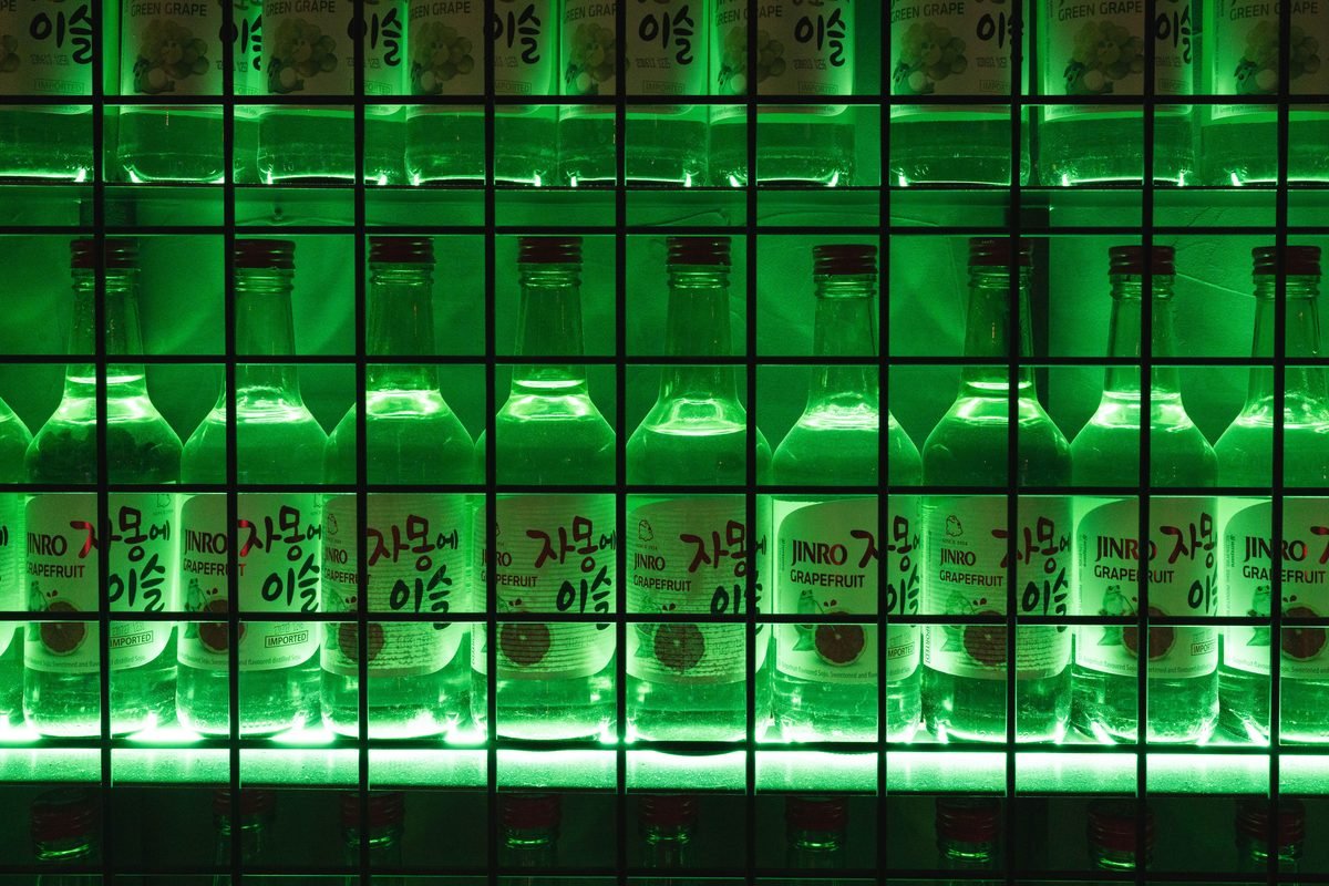 Illuminated green bottles of soju displayed on shelves