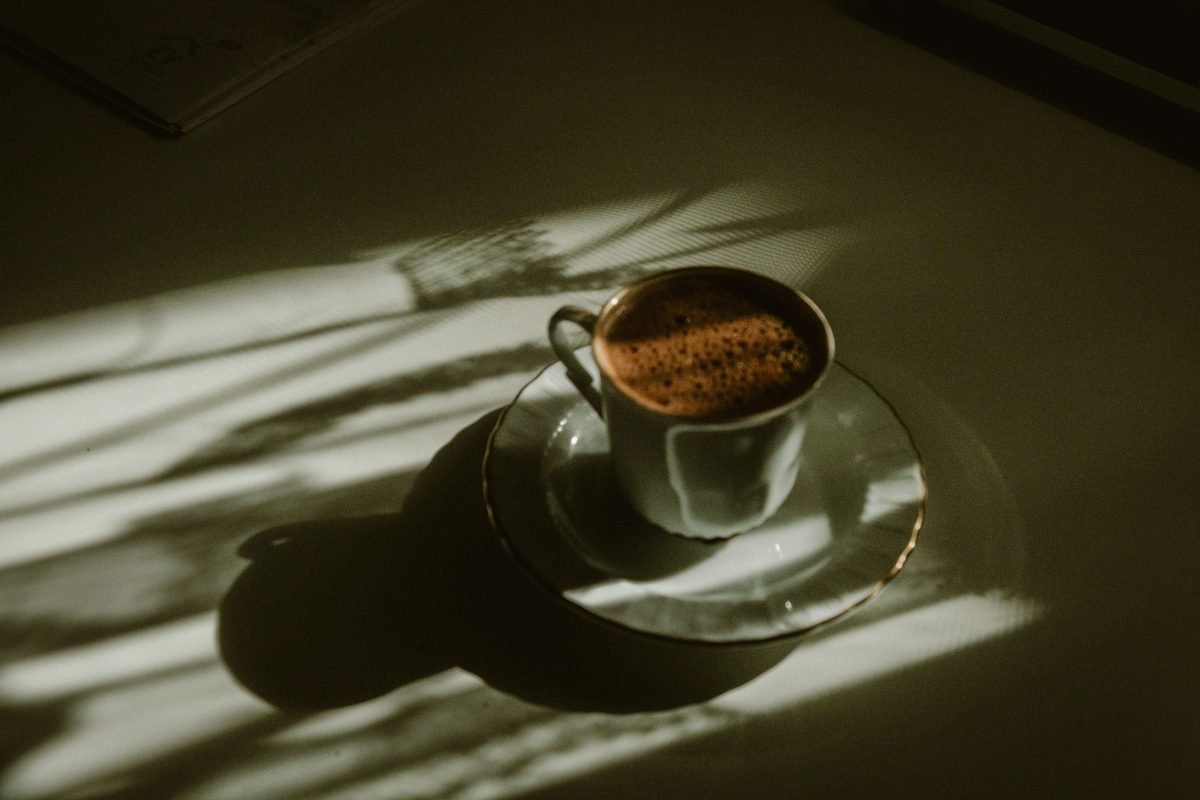 Artistic shot of a coffee cup on a table illuminated by soft sun rays.