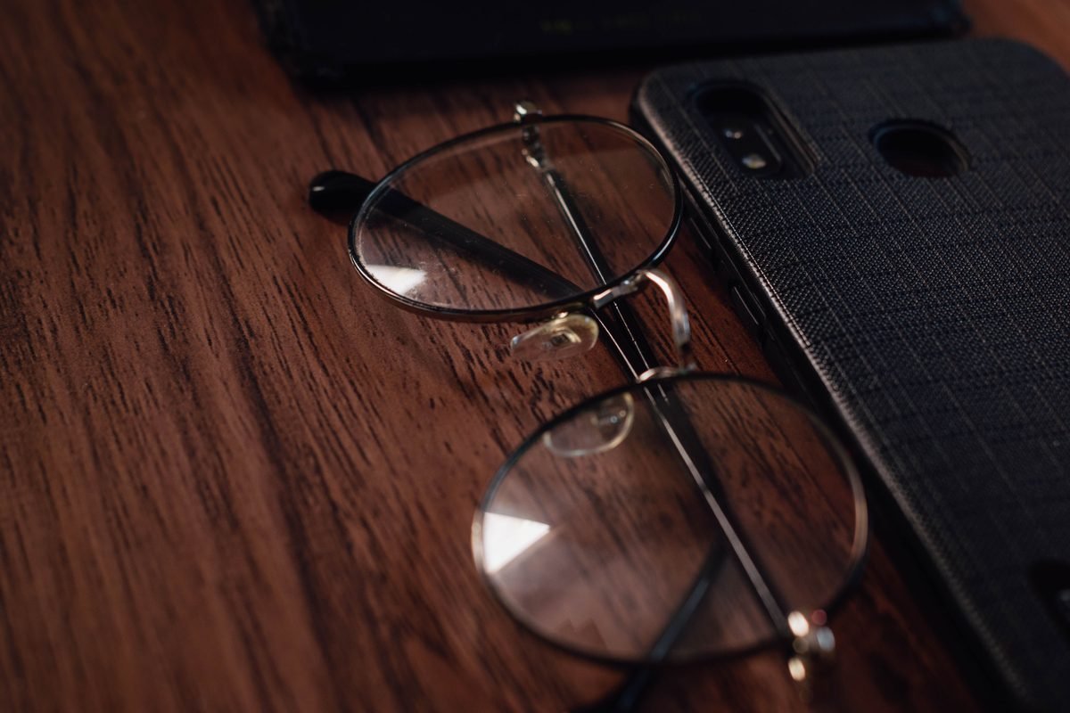 Smartphone and eyeglasses resting on a wooden table.
