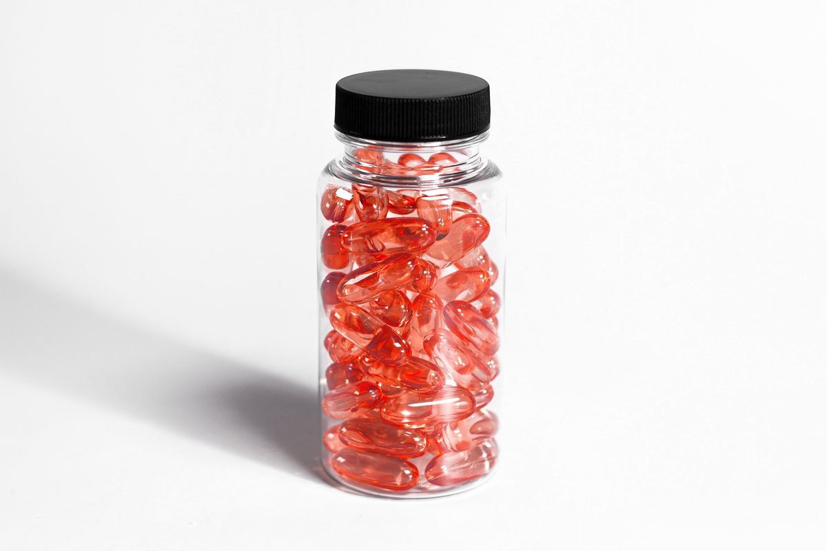 Clear jar filled with red capsules on a white background.