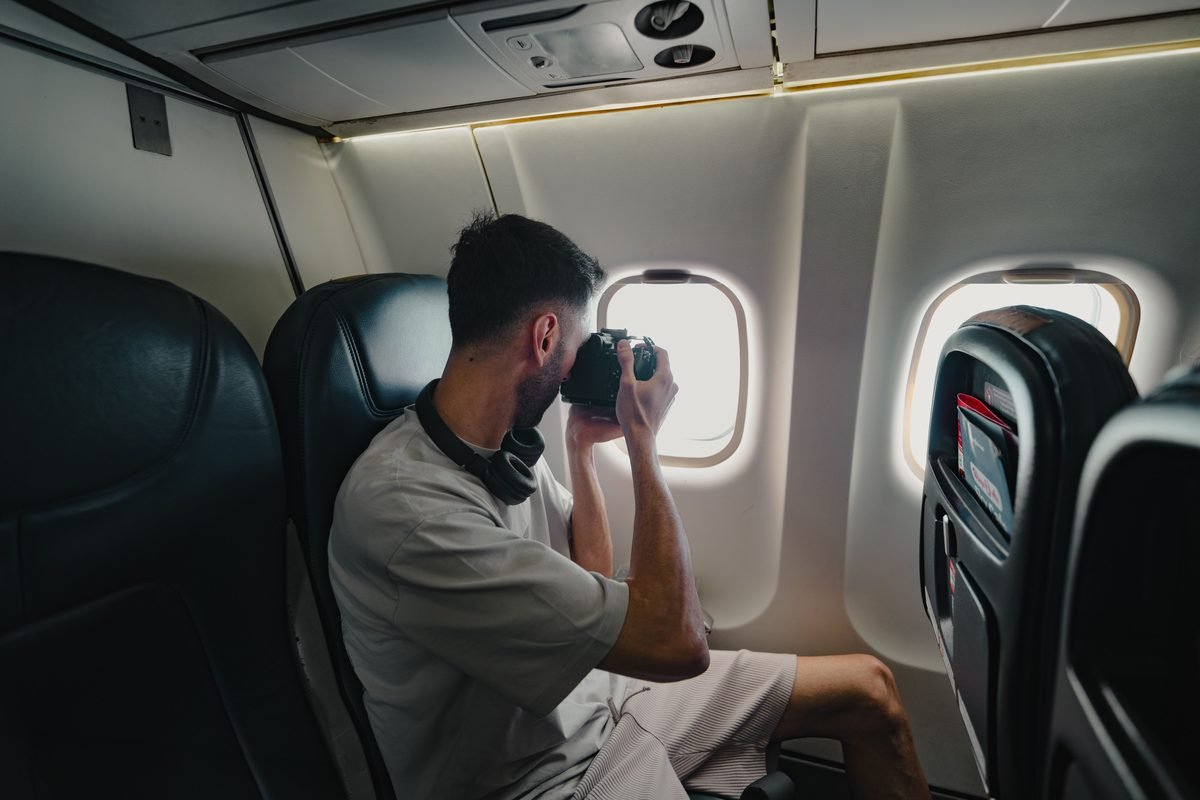 Traveler in an airplane using a camera to photograph through the window.