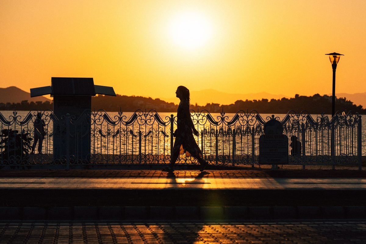 Silhouette of a woman walking at sunset by the waterfront.
